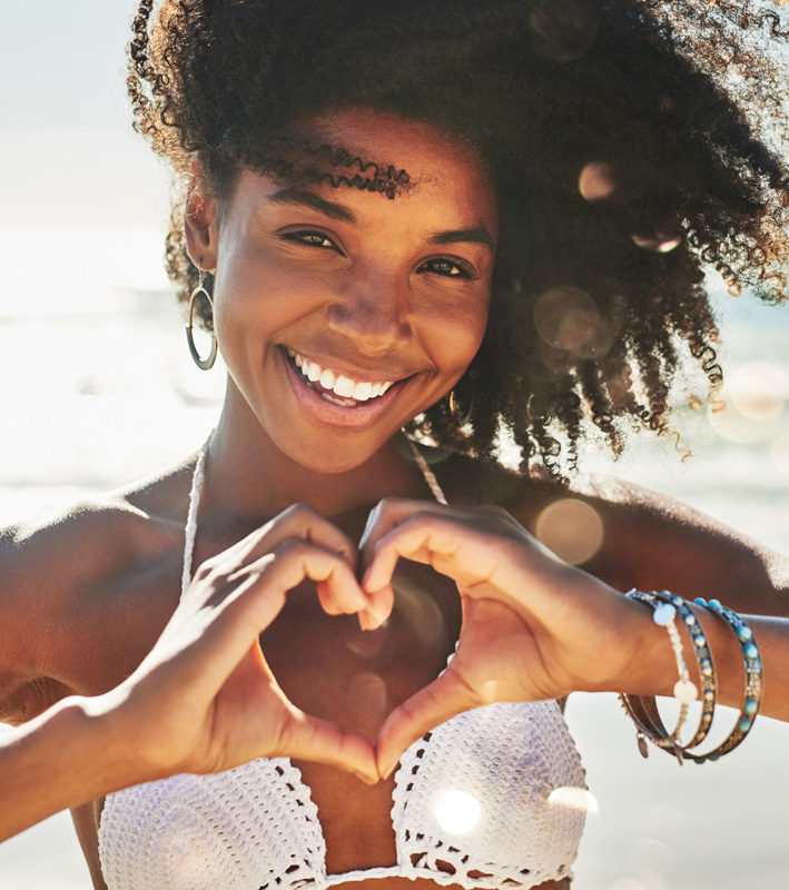My heart belongs to summer. Portrait of a beautiful young woman making a heart shaped gesture with her hands at the beach.