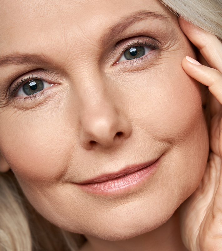 Happy attractive 50 years old middle aged mature woman touching healthy soft face skin looking at camera. Anti age dry skin care tightening treatment ads. Face close up view crop detail portrait